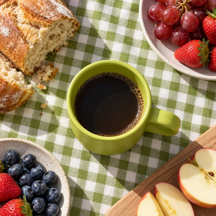 top-down: a matte lime mug on a gingham picnic blanket